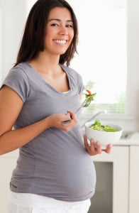 Pretty pregnant woman holding a bowl of salad while standing in the kitchen